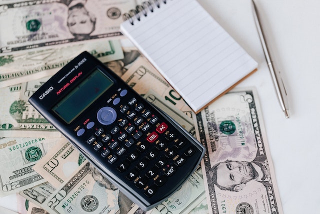 Graphing calculator and notepad on top of a pile of dollar bills